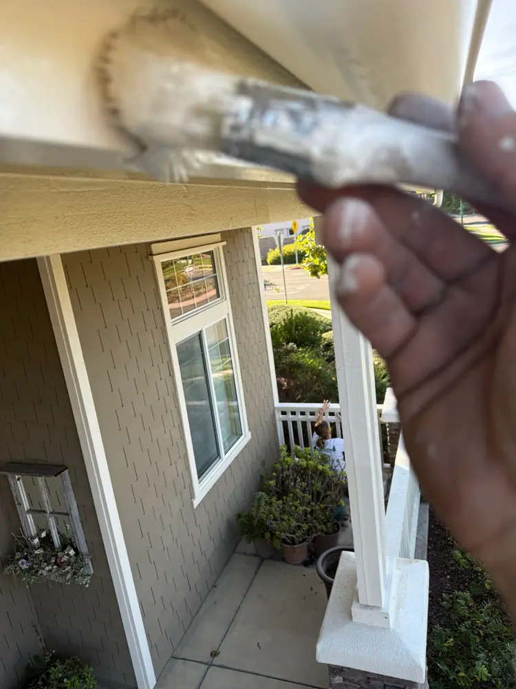 Painter's hand brushing a stucco eave and soffit line by hand on a Central Coast home