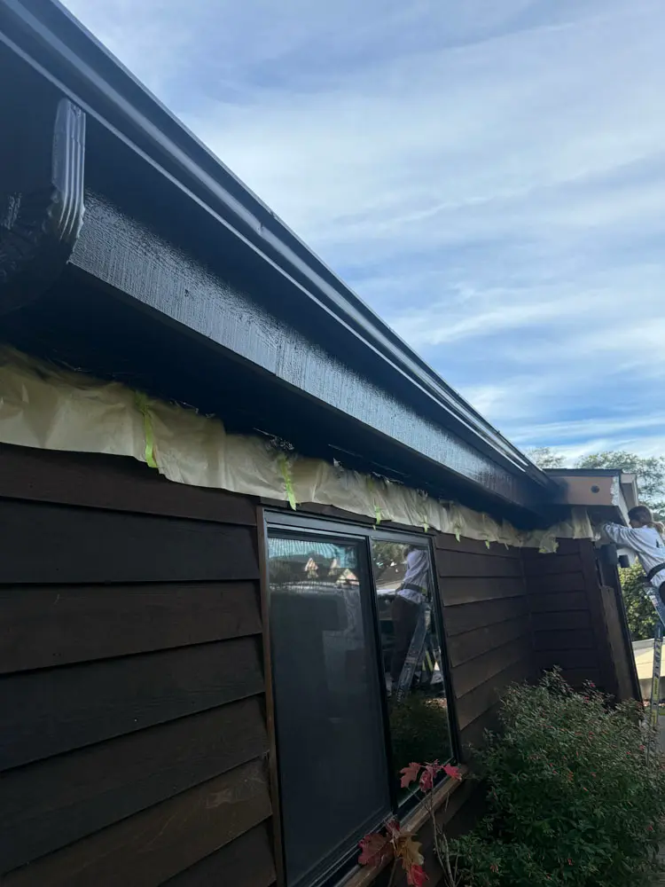 Freshly painted dark fascia board and gutter line with masking still in place along the siding