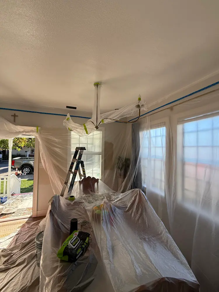 Interior room with furniture and fixtures fully covered in plastic sheeting before painting begins