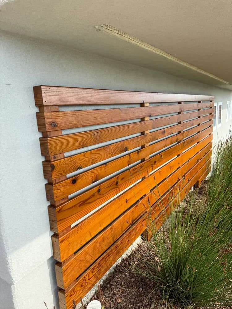 Stained horizontal cedar slat screen mounted against a pale stucco exterior wall